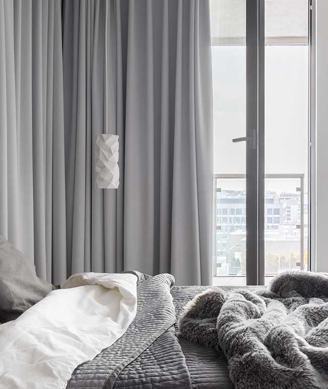 Imagen con sofa de un cuerpo gris con almohadones balncos y cortina blackout de gamuza gris y cortina de voile blanco.